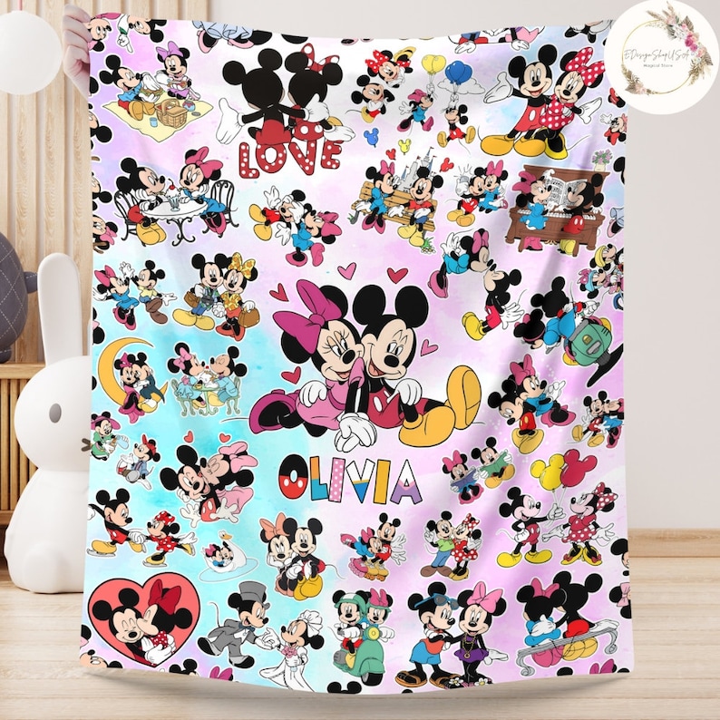 May include: A pink and blue patterned fleece blanket with a repeating pattern of Mickey Mouse and Minnie Mouse characters. The blanket features the word "LOVE" and the name "OLIVIA" in a colourful font.