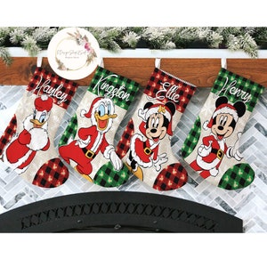 May include: Four Christmas stockings with personalized names: Hayley, Kingston, Ellie, and Henry. Each stocking features a different Disney character dressed in a Santa Claus outfit. The stockings have a red and black plaid pattern and a white background.