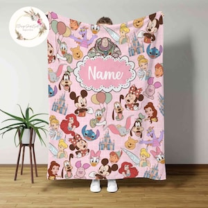May include: Pink fleece blanket with a pattern of various Disney characters, including Mickey Mouse, Minnie Mouse, Donald Duck, Goofy, and more. The blanket has a white grid pattern and a pink oval with the word "Name" in white text.
