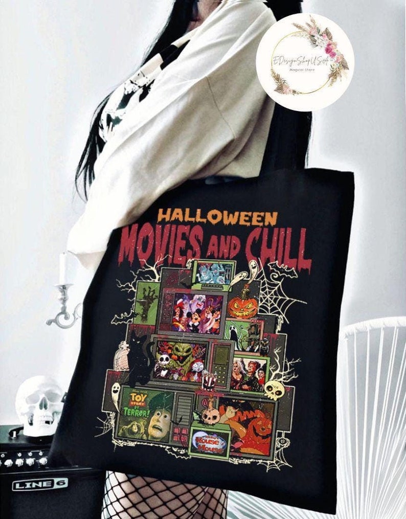May include: Black tote bag featuring a Halloween-themed design. The design includes the text "HALLOWEEN MOVIES AND CHILL" and various spooky movie scenes. A black cat, spiderwebs, and a jack-o'-lantern are also featured.