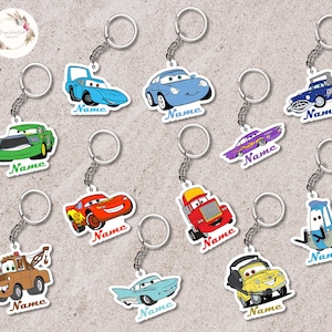 May include: A collection of cartoon car keychains in various colors, including blue, green, red, and yellow. Each keychain features a different car design with the word "Name" printed on a white label. The keychains are attached to silver key rings.