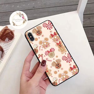 May include: A black phone case with a white background and a pattern of gingerbread cookies, candy canes, and red bows. The cookies are shaped like Mickey Mouse and Minnie Mouse.