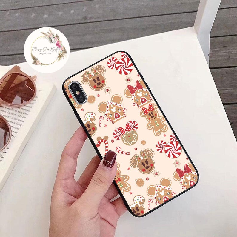 May include: A black phone case with a white background and a pattern of gingerbread cookies, candy canes, and red bows. The cookies are shaped like Mickey Mouse and Minnie Mouse.