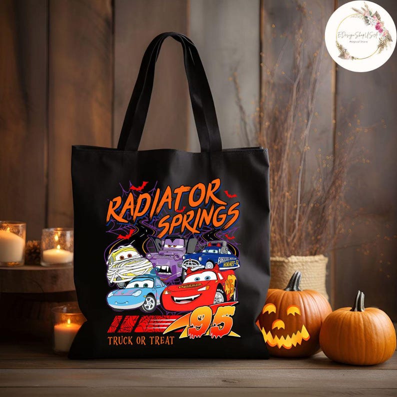 Op de afbeelding: Zwarte draagtas met een kleurrijke afbeelding van Cars-filmfiguren, de tekst "Radiator Springs" en "Truck or Treat". Het ontwerp bevat verschillende autokarakters en het nummer 95. Twee uitgesneden pompoenen en kaarsen op de achtergrond.
