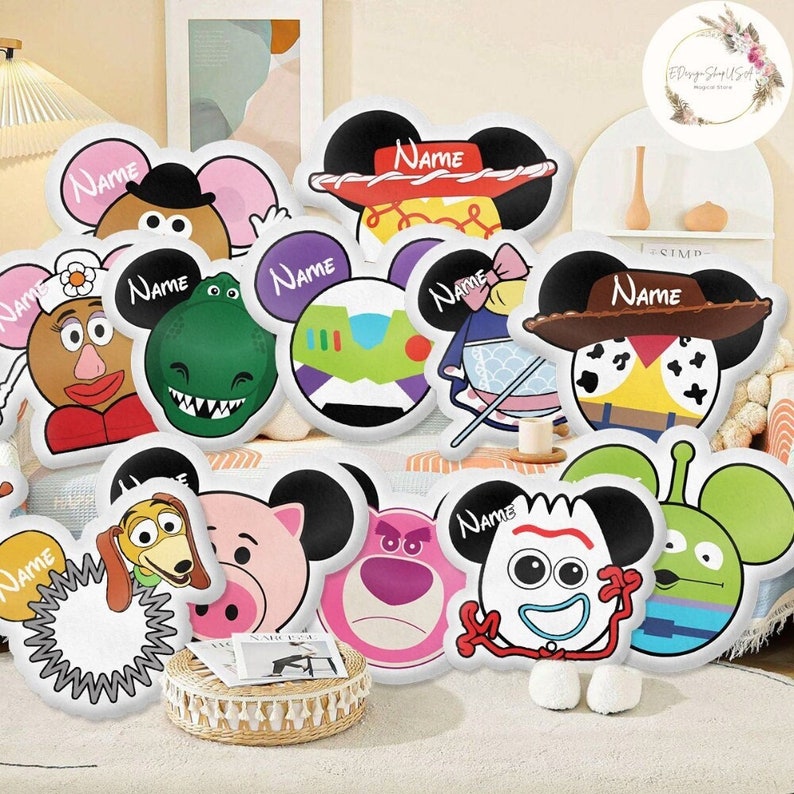 K&ouml;nnte beinhalten: Ein Set mit 10 wei&szlig;en Pl&uuml;schkissen mit verschiedenen Comicfiguren aus Disneys Toy Story von Pixar. Jedes Kissen hat eine Mickey-Maus-Ohrenform und das Wort "Name" ist darauf gedruckt. Die Figuren sind Woody, Buzz Lightyear, Rex, Mr. Potato Head, Hamm, Slinky Dog, Bo Peep, Jessie und Alien.
