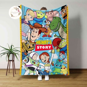 May include: A blue fleece blanket featuring a colourful illustration of characters from the Toy Story movie franchise. The blanket depicts Woody, Buzz Lightyear, Jessie, and other characters. The text "Disney Pixar Henry's Story" is printed on the blanket.