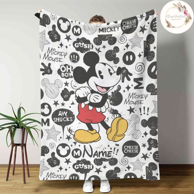Może przedstawiać: Czarno-biała kołdra z Mickey Mouse'em z wzorem bazgroł&oacute;w. Kołdra przedstawia Mickey Mouse'a w jego charakterystycznych czerwonych spodenkach i ż&oacute;łtych butach. Wz&oacute;r zawiera głowę Mickey Mouse'a, gwiazdki i słowa "Mickey Mouse", "Oh Boy", "Aw Shucks", "Gush", "Name" i "Cheese Cheese".