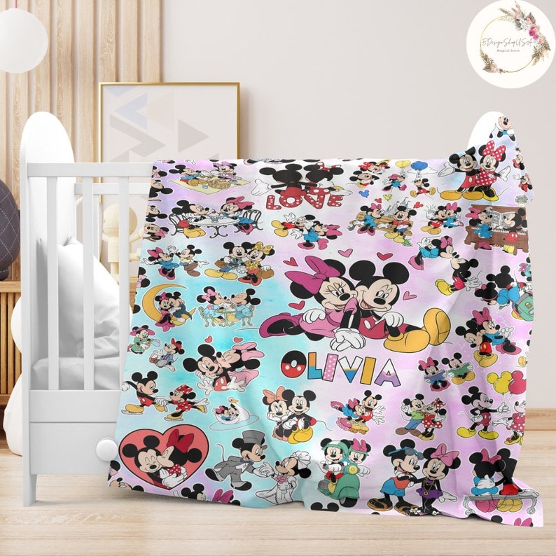 May include: A pink and blue blanket with a colourful pattern of Mickey Mouse and Minnie Mouse characters. The blanket features the word "LOVE" and the name "OLIVIA" in a pink and blue font.