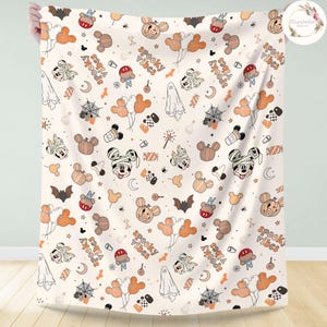 May include: A white fabric blanket with a Halloween-themed pattern featuring Mickey Mouse in a mummy costume, pumpkins, bats, ghosts, and the text "spooky vibes".
