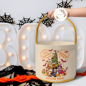 May include: A beige canvas trick-or-treat bag with a yellow handle. The bag features a Mickey Mouse Halloween party design with the text "Mickey's Not So Scary Halloween Party" and "2024". The bag also has a space for a custom name.