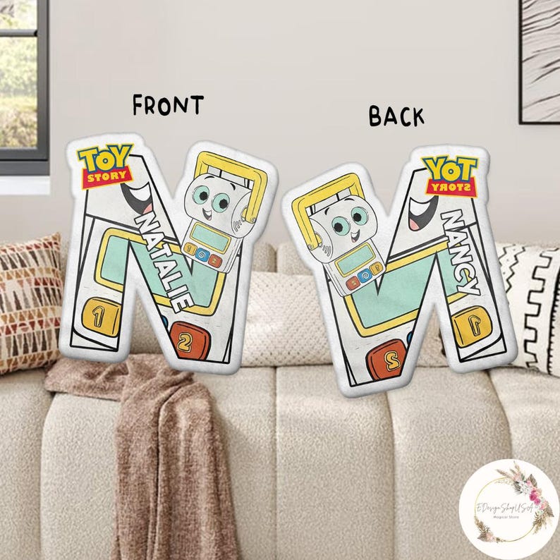 May include: Two decorative pillows shaped like the letter "N". The front pillow has the text "NATALIE" and the "Toy Story" logo. The back pillow has the text "NANCY" and the "YOT YROTZ" logo. Each pillow features a cartoon character.