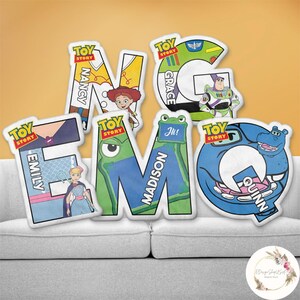 May include: A collection of colorful, letter-shaped pillows featuring characters and text from the "Toy Story" franchise. Each pillow displays a different letter, with names like "Nancy," "Emily," "Madison," "Grace," and "Quinn" incorporated into the designs.