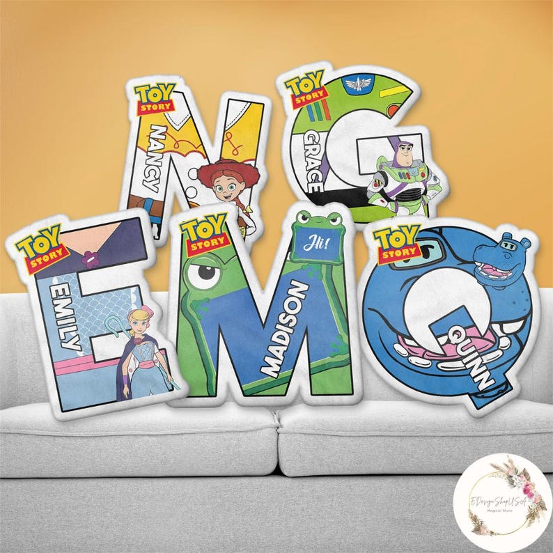 May include: A collection of colorful, letter-shaped pillows featuring characters and text from the "Toy Story" franchise. Each pillow displays a different letter, with names like "Nancy," "Emily," "Madison," "Grace," and "Quinn" incorporated into the designs.