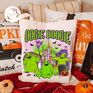 Puede incluir: Una bolsa de lona blanca con un estampado gr&aacute;fico verde, morado y negro de Oogie Boogie de Pesadilla antes de Navidad. El gr&aacute;fico presenta a Oogie Boogie frente a un castillo con murci&eacute;lagos volando alrededor.