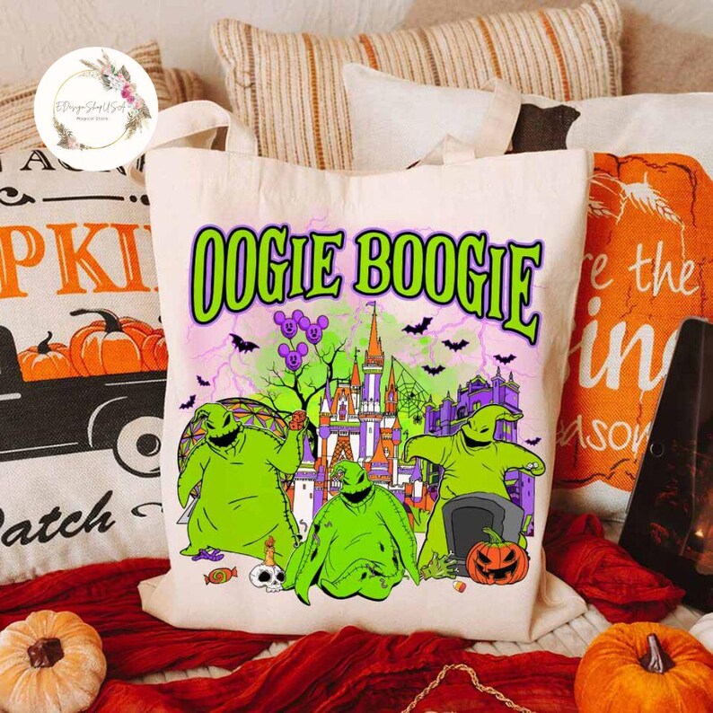 Puede incluir: Una bolsa de lona blanca con un estampado gr&aacute;fico verde, morado y negro de Oogie Boogie de Pesadilla antes de Navidad. El gr&aacute;fico presenta a Oogie Boogie frente a un castillo con murci&eacute;lagos volando alrededor.