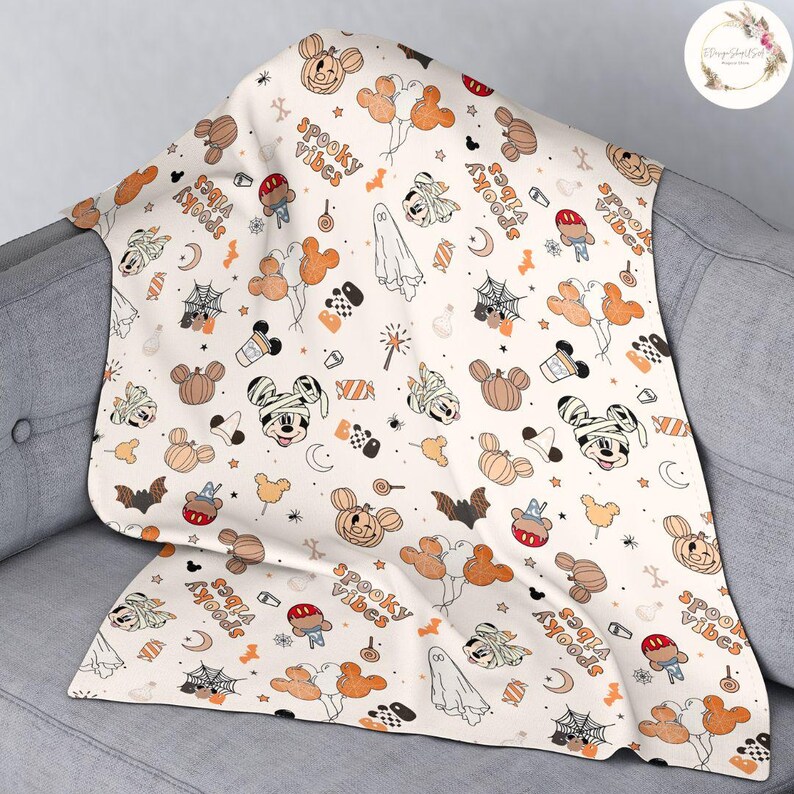 May include: A white fleece blanket with a Halloween-themed pattern featuring Mickey Mouse and the phrase "Spooky Vibes". The pattern includes Mickey Mouse in various poses, pumpkins, bats, candy corn, and spiderwebs.