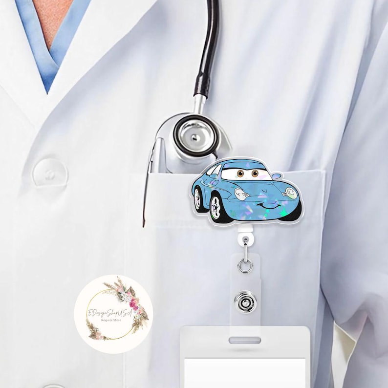 Puede incluir: Un portatarjetas en forma de coche azul claro con una cara sonriente y ojos grandes. El portatarjetas est&aacute; sujeto a un cord&oacute;n blanco y se engancha a un bolsillo blanco. Un accesorio divertido para profesionales m&eacute;dicos.