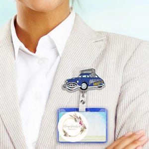 Puede incluir: Un portatarjetas retr&aacute;ctil azul y blanco con tem&aacute;tica de Cars, con un dise&ntilde;o de coche de dibujos animados y el texto "Farley's Museum of Hornet-5". El portatarjetas est&aacute; unido a un soporte de identificaci&oacute;n azul con un dise&ntilde;o floral.