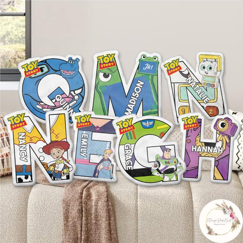 May include: A collection of colorful Toy Story-themed letter pillows. Each letter features a different character and name, including "Quinn," "Madison," "Natalie," "Nancy," "Emily," "Grace," and "Hannah." The pillows are displayed on a beige sofa.