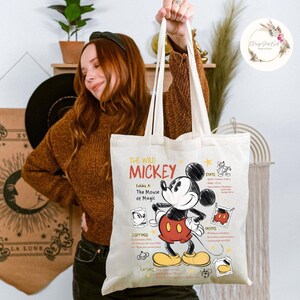 May include: Cream-colored tote bag featuring a graphic of Mickey Mouse with the text "THE WILD MICKEY". The bag includes details about Mickey's stats, sightings, and features. The bag has long, cream-colored handles.