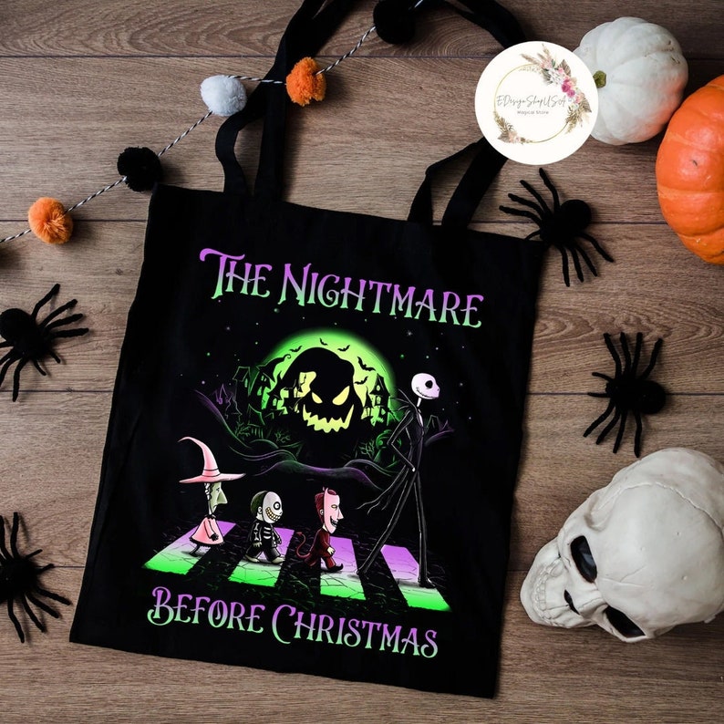 K&ouml;nnte beinhalten: Schwarze Tragetasche mit einem Grafikmotiv aus "The Nightmare Before Christmas". Das Design zeigt Jack Skellington und andere Charaktere, die einen Zebrastreifen &uuml;berqueren, mit dem Text "The Nightmare Before Christmas". Dekorative Spinnen, K&uuml;rbisse und ein Totenkopf umgeben die Tasche.