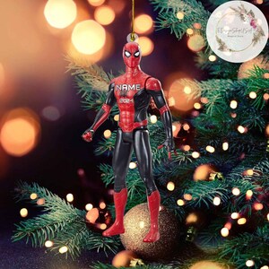K&ouml;nnte beinhalten: Ein roter und schwarzer Spider-Man Weihnachtsbaumschmuck mit dem Text "NAME 2024" auf der Brust. Der Schmuck h&auml;ngt an einem Weihnachtsbaum.