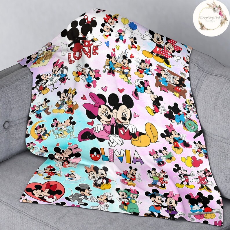 May include: A pink and blue blanket with a repeating pattern of Mickey Mouse and Minnie Mouse. The blanket features a variety of images of the characters, including them holding hands, playing music, and kissing. The blanket also features the word "LOVE" and the name "OLIVIA".