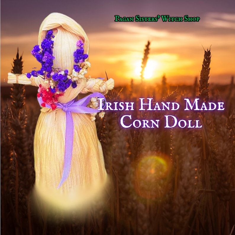 May include: A handmade corn husk doll with purple and red flowers, a purple ribbon, and the text "Irish Hand Made Corn Doll" in a field of tall grass at sunset.