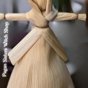 May include: A handmade corn husk doll with a long, flowing dress and a hood. The doll is tied with twine at the waist and has a simple, rustic look.