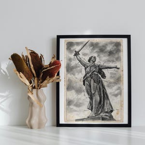 May include: Black framed print featuring a detailed illustration of a statue holding a sword, with architectural diagrams overlaid. The artwork is in grayscale, set against a cloudy sky background. A beige vase with dried flowers is to the left.