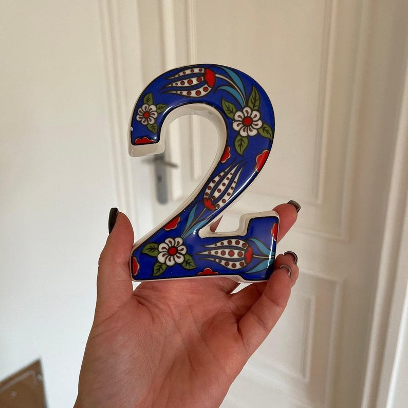 May include: A blue and white ceramic number two with a floral design. The number is decorated with red, white, and blue flowers.