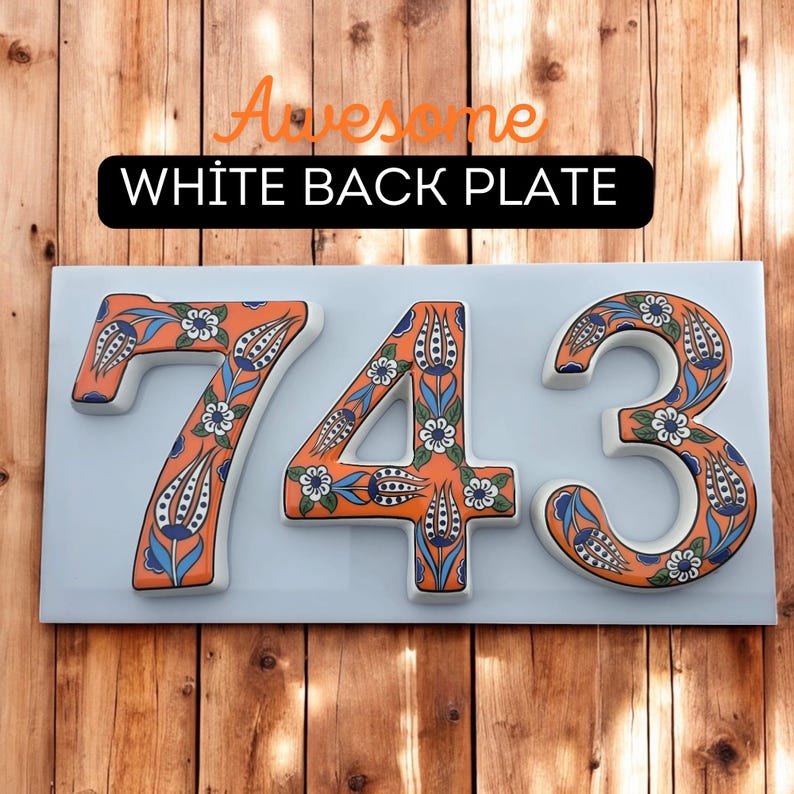 May include: A white ceramic house number sign with the numbers 743 in orange and blue floral designs. The sign is mounted on a wooden surface.