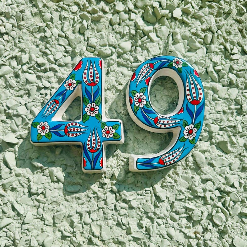 May include: Ceramic house number 49 with a blue background and white and red floral design.