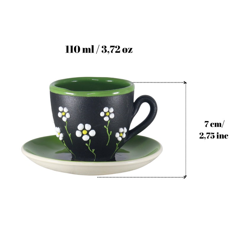 May include: Black and green ceramic coffee cup and saucer set with white daisy flower designs. The cup holds 3.72 ounces or 110 milliliters. The saucer is 7 inches or 17.78 centimeters in diameter.