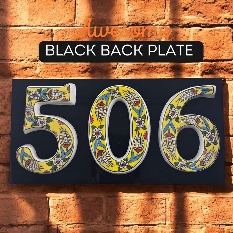 May include: A black ceramic house number plaque with white, yellow, blue, and red floral designs. The numbers 506 are displayed on the plaque.