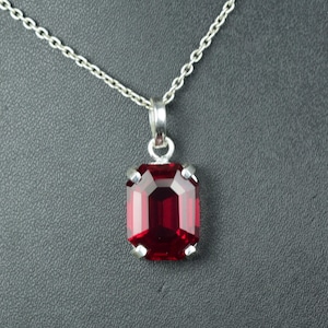May include: A silver necklace featuring a rectangular, faceted, deep red pendant. The pendant is set in a silver bezel and hangs from a delicate silver chain. The pendant's color is a rich, vibrant red.