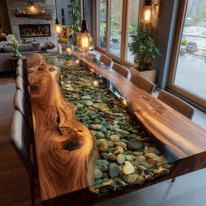 May include: A long dining table featuring two thick, natural-edge walnut wood slabs separated by a central glass-topped channel filled with smooth, multi-colored river stones. The table is surrounded by several upholstered dining chairs.