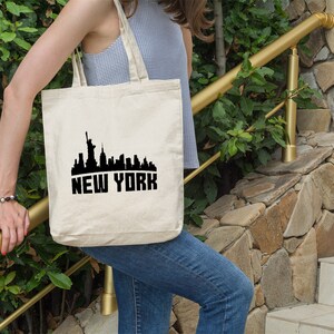 May include: A white canvas tote bag with a black silhouette of the New York City skyline and the text "NEW YORK" printed on the front.
