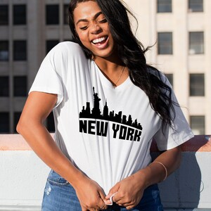May include: A white t-shirt with a black graphic of the New York City skyline, including the Statue of Liberty. The text "NEW YORK" is printed below the skyline.