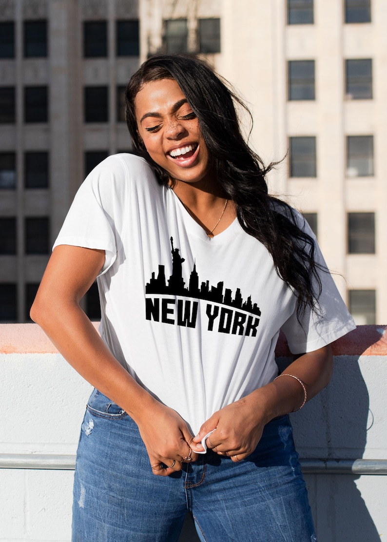 May include: A white t-shirt with a black graphic of the New York City skyline, including the Statue of Liberty. The text "NEW YORK" is printed below the skyline.