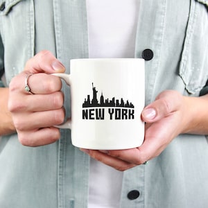 May include: White ceramic mug with a black silhouette of the New York City skyline and the text "NEW YORK" printed on the front.