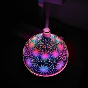 May include: A round, white ceramic essential oil diffuser with a colourful, abstract design. The diffuser has a light that changes colours and emits a fine mist.