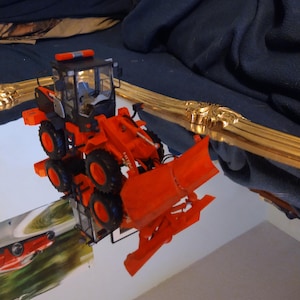 May include: A red and black toy construction vehicle with a front loader and a flashing light on top. The vehicle is sitting on a mirrored surface.