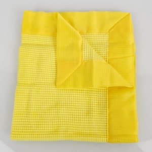 May include: A yellow waffle weave baby blanket with a folded corner. The blanket has a yellow border.