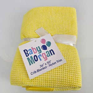 May include: Yellow waffle weave crib blanket with a white satin ribbon and a tag that reads "Baby Morgan 36" x 50" Crib Blanket - Nylon Trim".
