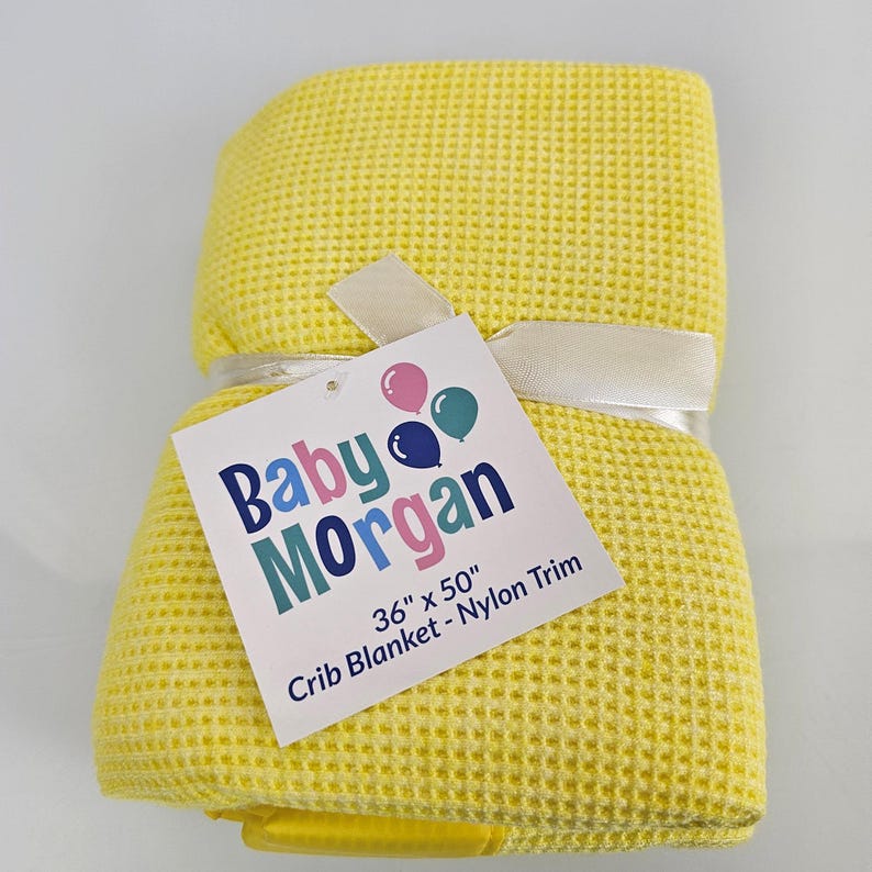 May include: Yellow waffle weave crib blanket with a white satin ribbon and a tag that reads "Baby Morgan 36" x 50" Crib Blanket - Nylon Trim".