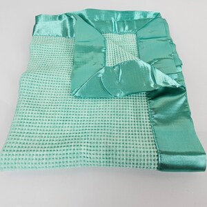 May include: A soft, light green waffle weave baby blanket with a satin trim. The blanket is folded in half and the satin trim is visible on all four sides.