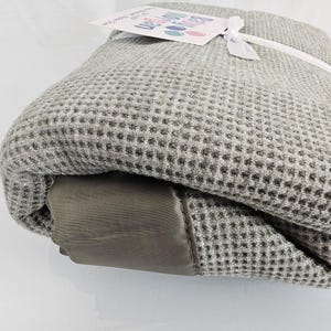 May include: A gray waffle weave throw blanket with a brown leather-like trim. The blanket is rolled up and tied with a white ribbon. A tag with the text "Beyond the Moon" is attached to the ribbon.