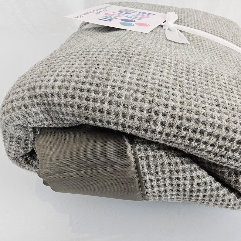 May include: A gray waffle weave throw blanket with a brown leather-like trim. The blanket is rolled up and tied with a white ribbon. A tag with the text "Beyond the Moon" is attached to the ribbon.