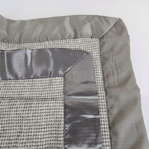 May include: A gray waffle weave throw blanket with a satin trim. The blanket has a subtle pattern of small squares.